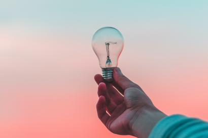 Arm of a light skinned person holding a lightbulb against a blue and pink sunset