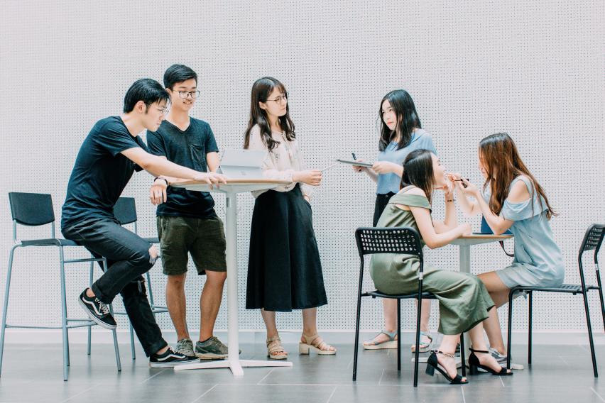 Six students sit and stand around classroom desks.