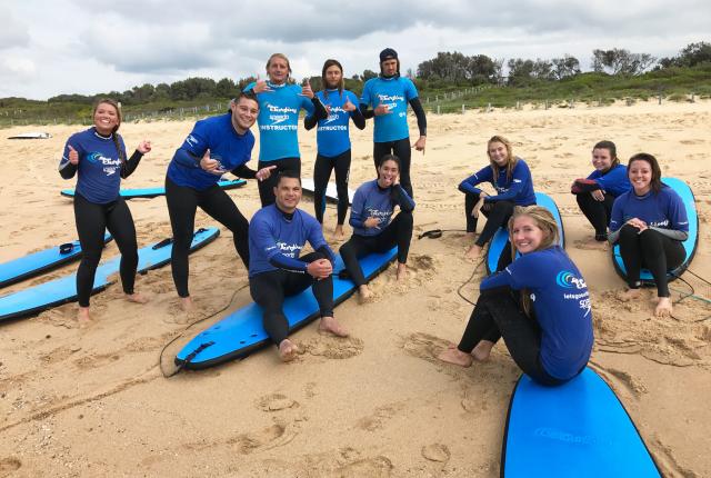 a group of students pose for a photo with their surf boards and surf gear on the beach in Sydney