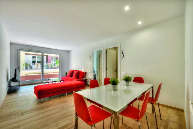 A minimalist living space featuring bright red furniture, a large window, a television, and a dining room with red chairs.