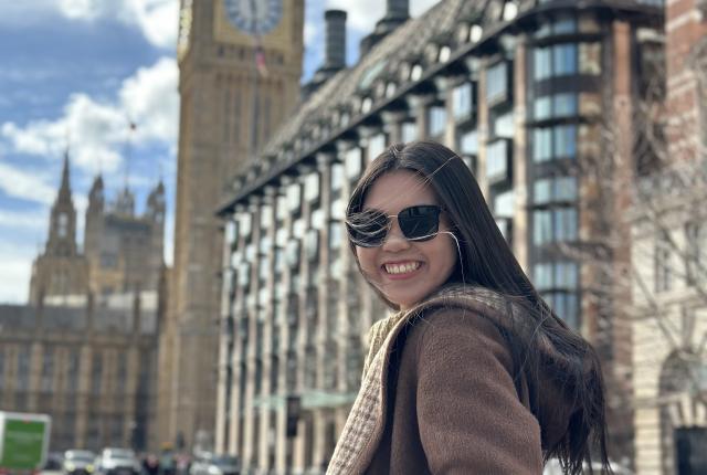 student in jacket and sunglasses walking down a sunny sidewalk towards big ben