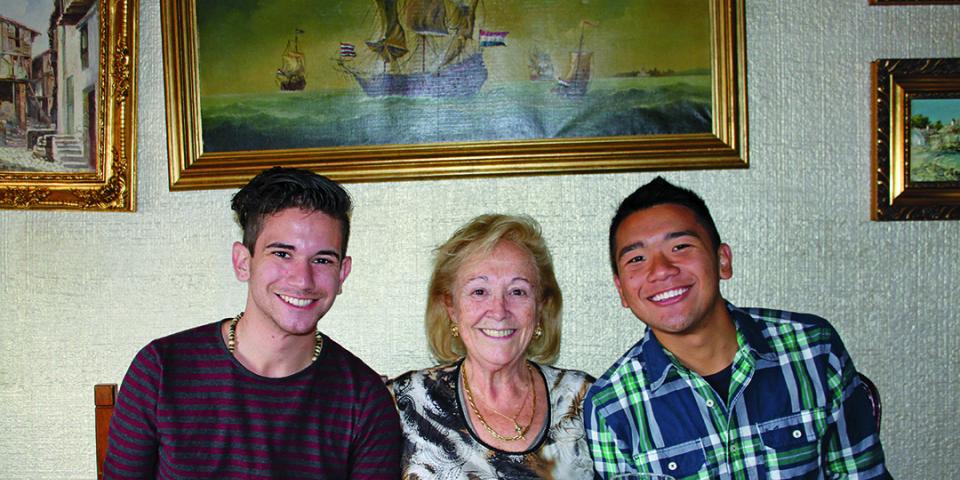 Students sit with their host mother at the dinner table, smiling at the camera.